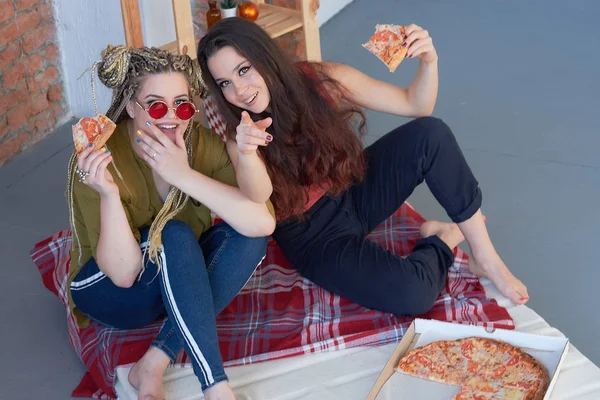 two girls eat pizza in the room on the bed. junk food.