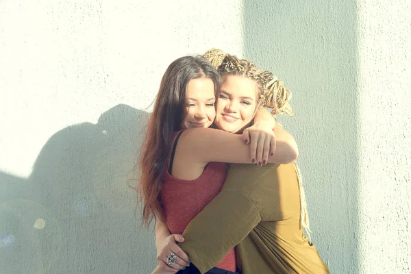 best friends hugging against a white wall. bright sunlight, contrast light.