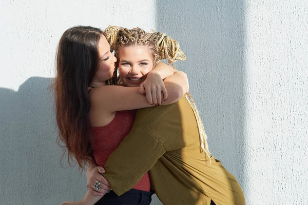 best friends hugging against a white wall. bright sunlight, contrast light.