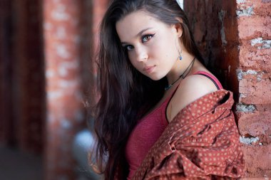 uzun saçlı Genç esmer kadın tuğla duvara yakın duruyor.