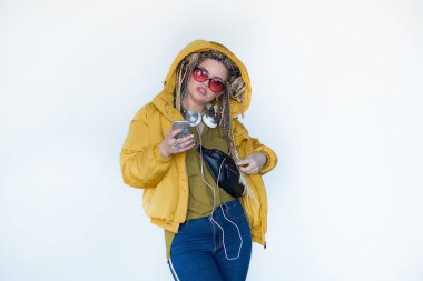 Genç sarışın kız güneş gözlüğü ile Afrika pigtails içinde kulaklık ve beyaz bir arka plan müzik dinler.