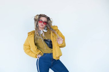 Genç sarışın kız güneş gözlüğü ile Afrika pigtails içinde kulaklık ve beyaz bir arka plan müzik dinler.