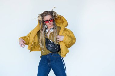 Genç sarışın kız güneş gözlüğü ile Afrika pigtails içinde kulaklık ve beyaz bir arka plan müzik dinler.