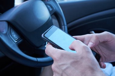 Asyalı adam araba sürerken elinde mesajlaşma cep telefonu ile arabada oturan