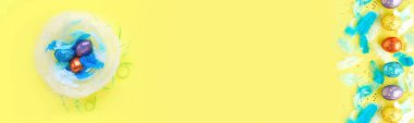 mavi tüyleri, tavşan kulakları ve ahşap tavşan oyuncakları ile bir yuvada paskalya yumurtaları için renkli arka plan. tatil hazırlık konsepti. sarı bir arka plan, pastel renkler. tatil davranır sepeti.
