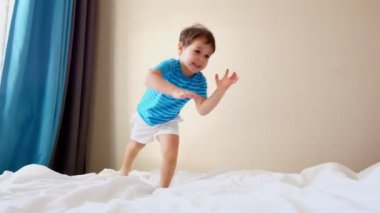komik çocuk preschooler masmavi t-shirt beyaz atlar büyük yumuşak anne yatakta falls ağır çekim gülümseyen düz şort.