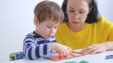 küçük Asyalı Oğlan masada oturan anne ile bulmacalar toplar. Sevimli bir çocuk büyük çok renkli detaylardan bir resim toplar. yavaş hareket. Öğretmen oyun ile çocuk içinde Montessori sınıf