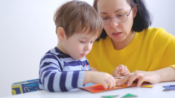 Petit garçon asiatique recueille des puzzles avec maman assise au bureau. Un enfant mignon recueille une image à partir de grands détails multicolores. au ralenti. Professeur jouant avec le garçon en classe montessori — Video