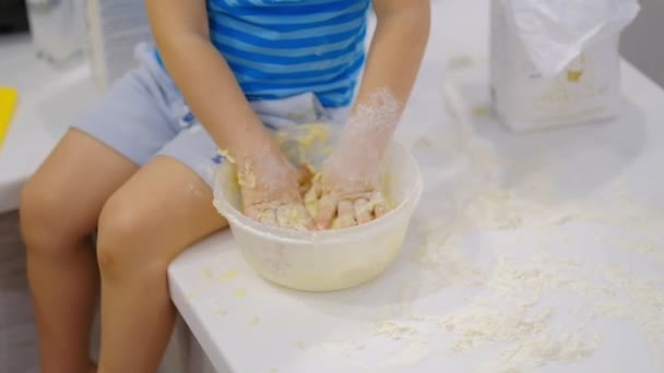 小さな子供がテーブルの上に生地を準備し、くしゃみをします。小麦粉で遊んでいる小さな赤ちゃん。ベイカーが生地を準備する — ストック動画