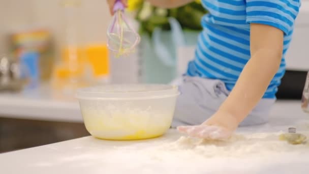 小さな子供がテーブルの上に生地を準備し、くしゃみをします。小麦粉で遊んでいる小さな赤ちゃん。ベイカーが生地を準備する — ストック動画