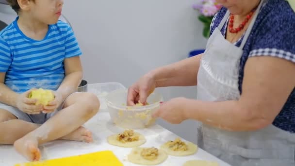 Close-up van de gelukkige glimlach grootmoeder en kleinzoon kneden een dochters samen. Slow Motion van een oudere vrouw en kleine jongen bereiden pasta of pizza samen. — Stockvideo