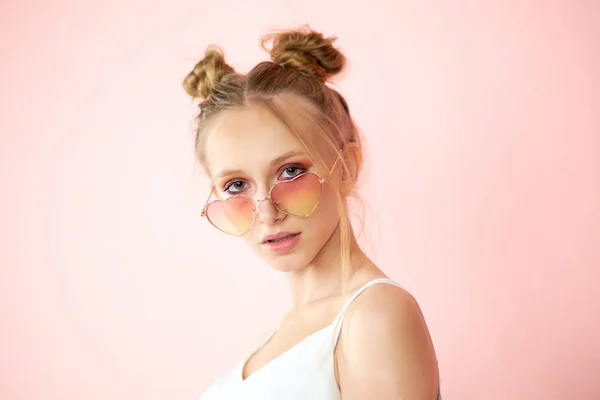 Rosto de uma jovem em óculos cor-de-rosa na forma de um coração. retrato de uma mulher bonita em um fundo rosa — Fotografia de Stock