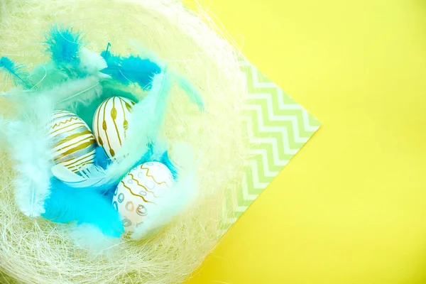 Kleurrijke achtergrond voor Pasen, eieren in een nest met blauwe veren — Stockfoto