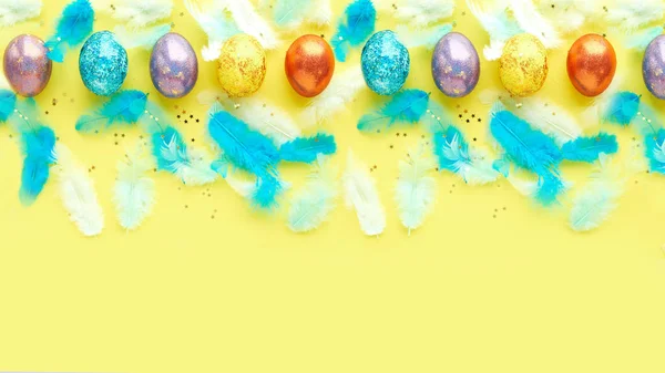 Cuadrado de huevos de Pascua sobre un fondo amarillo. plumas azules dispersas. banner para texto — Foto de Stock