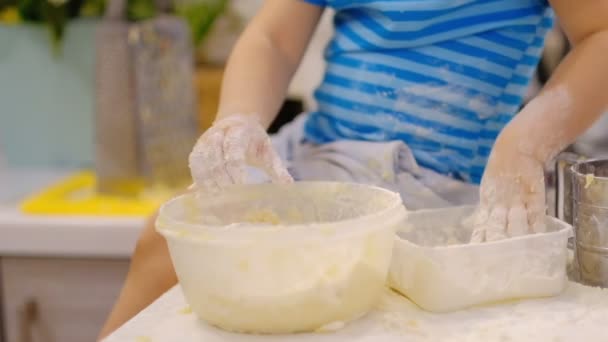 小さな子供がテーブルの上に生地を準備し、くしゃみをします。小麦粉で遊んでいる小さな赤ちゃん。ベイカーが生地を準備する — ストック動画