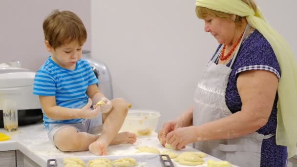 Großaufnahme der glücklich lächelnden Großmutter und des Enkels, die eine Tochter zusammen kneten. Zeitlupe einer älteren Frau und eines kleinen Jungen, die gemeinsam Pasta oder Pizza zubereiten. — Stockvideo