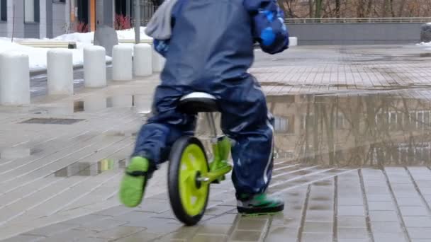 Fermez au ralenti. Petit garçon joue dans une flaque de boue. Un enfant en vélo pour enfants à travers les flaques d'eau. début du printemps — Video