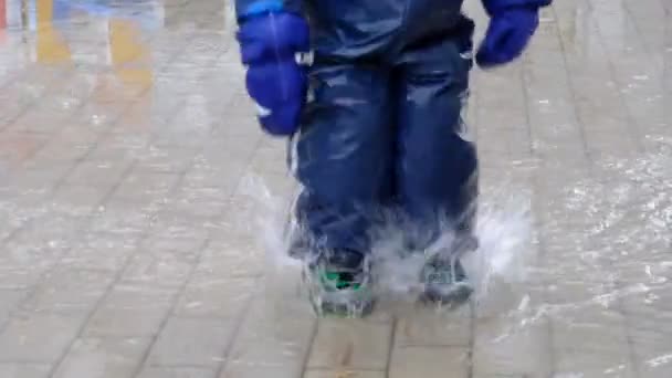 Крупный план замедленной съемки ног мальчика, прыгающего в грязную лужу, делая всплеск. резиновые сапоги, счастливого детства — стоковое видео