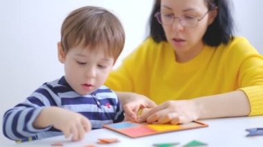 küçük asyalı çocuk masada oturan anne ile bulmaca toplar. Sevimli bir çocuk büyük çok renkli ayrıntılardan bir resim toplar. Bir bulmaca yla oynuyorum. yavaş çekim. Öğretmen çocukla oynuyor