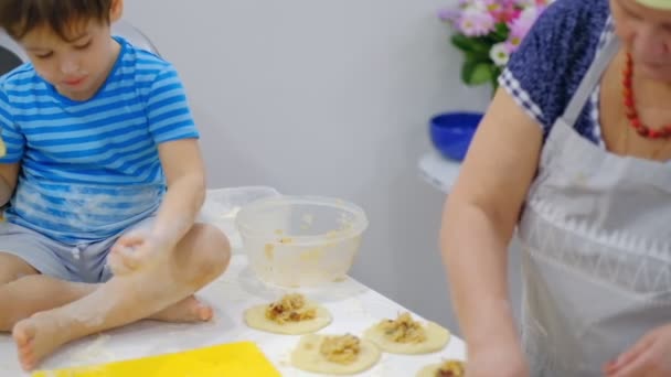 Großaufnahme der glücklich lächelnden Großmutter und des Enkels, die eine Tochter zusammen kneten. Zeitlupe einer älteren Frau und eines kleinen Jungen, die gemeinsam Pasta oder Pizza zubereiten. — Stockvideo