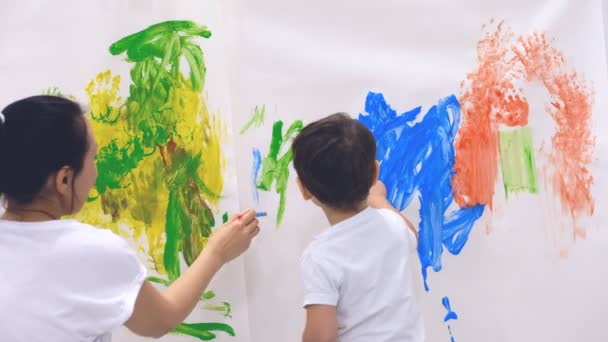 Primer plano de niño feliz haciendo colorido handsprint en la pared blanca con la madre juntos. Movimiento lento — Vídeo de stock