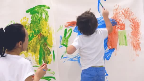 Close-up de criança pequena feliz fazendo colorido handsprint na parede branca com a mãe juntos. Movimento lento — Vídeo de Stock