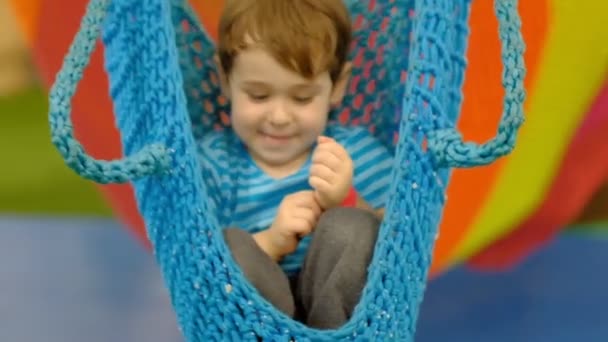 Sad boy three years old, swinging on a swing alone in the childrens room. lonely child without friends — Stock Video