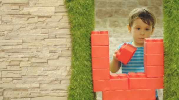 Αγόρι είναι τριών ετών, παίζει μόνος στο παιδικό δωμάτιο, στέκεται ένα τείχος από μεγάλα πλαστικά τουβλάκια. — Αρχείο Βίντεο