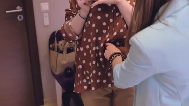 Woman shop assistant helps lady try on brown polka dot blouse and beige trousers in store close view slow motion — Stock Video