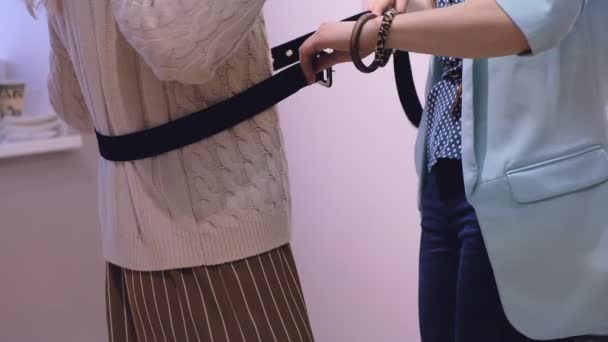 Verkäuferin hilft Dame im beigen Pullover beim Anziehen und Ausziehen des Ledergürtels in Zeitlupe in der Umkleidekabine — Stockvideo