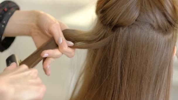 Eine Friseurin macht einer Kundin eine voluminöse Frisur mit einem Haarbügler, der die Haare kräuselt. professioneller Friseur bei der Arbeit. Zeitlupe — Stockvideo