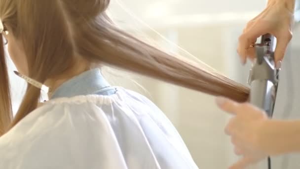 Eine Friseurin macht einer Kundin eine voluminöse Frisur mit einem Haarbügler, der die Haare kräuselt. professioneller Friseur bei der Arbeit. Zeitlupe — Stockvideo