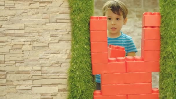 Jongen is drie jaar oud, speelt alleen in de kinderkamer, staat een muur van grote kunststof blokken. — Stockvideo