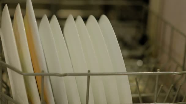 Kadınlar bulaşık makinesinden tabak toplarlar. Bulaşık makinesini boşaltan kadın. Temiz aletler raflarda dizilir. Kadın ev mutfağında çalışıyor.. — Stok video