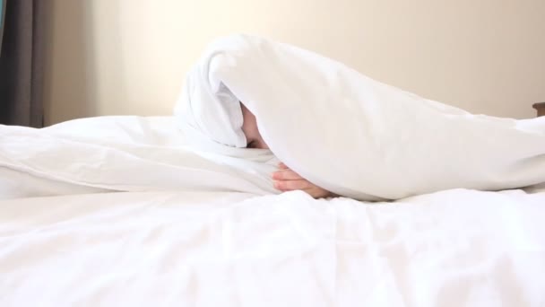 Engraçado menino espreita sob sorrisos cobertor macio e cobre cobertor com cabeça em pais grandes cama câmera lenta — Vídeo de Stock