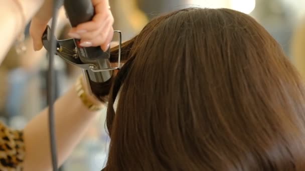 Женщина парикмахер делает объемную прическу клиенту с помощью утюга, обжига волос. Профессиональный парикмахер. замедленное движение — стоковое видео