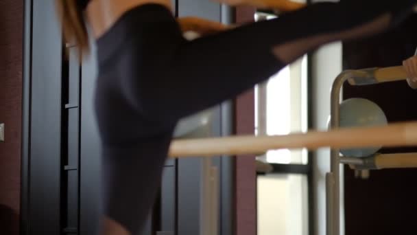 Gadis cantik fleksibel dengan ekor kuda di atas hitam membungkuk tubuh ke belakang dengan kaki di pegangan balet closeup gerakan lambat — Stok Video