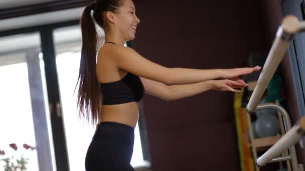 Темноволосая девушка профессиональный танцор в верхней и колготки показывает балетные движения руки держа перила медленное движение — стоковое видео