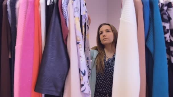 Portrait of a young charming woman finding herself new clothes in a expensive boutique. She is reading tags and choosing. — Stock Video