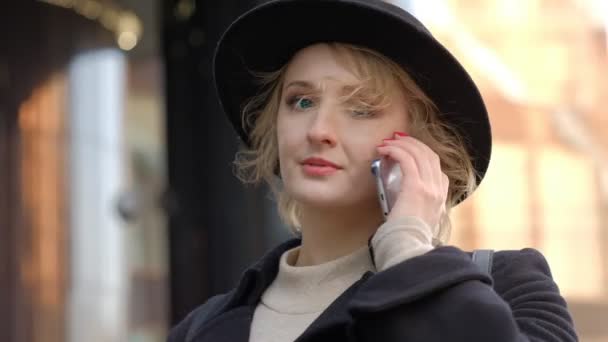 Nice girl in black hat smiles talking on smartphone closeup — Stock Video