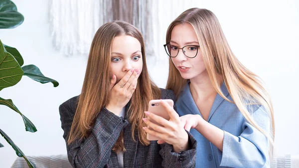 Due donne a casa guardando il cellulare e sorridendo. Amici che guardano un telefono cellulare — Foto Stock