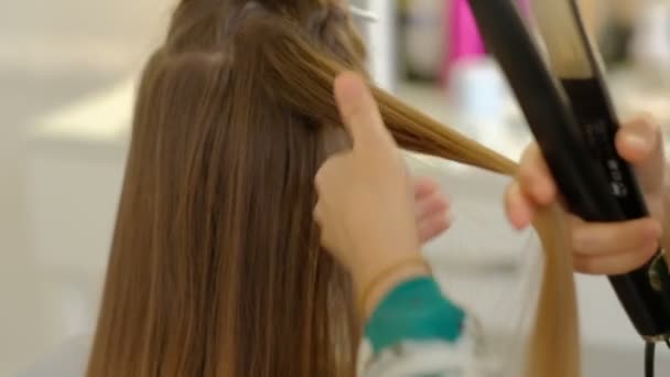 Uma mulher cabeleireira faz um penteado volumoso para um cliente usando uma máquina de passar o cabelo, frisando o cabelo. Cabeleireiro profissional no trabalho. câmara lenta — Vídeo de Stock