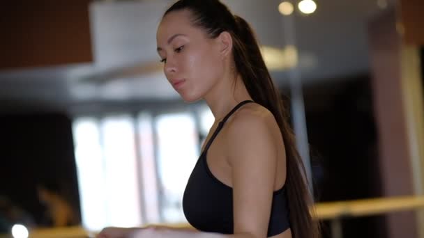 At kuyruklu siyah saçlı kız dansçı bale makinesi korkuluk eğilir ve yakın yan görünümü yavaş hareket dinlenir — Stok video