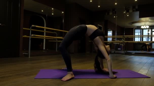 Young woman with ponytail shows body flexibility doing exercise bridge bending over backwards on floor slow motion — 비디오