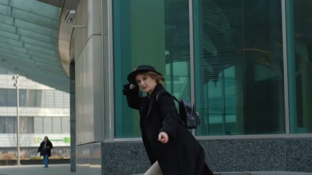 Blond tjej med ryggsäck promenader sätta på hatt i gatan — Stockvideo