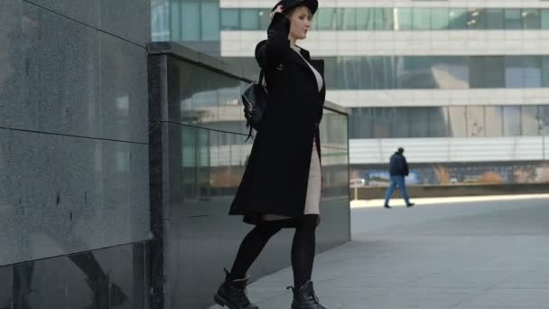 Chica rubia con mochila camina poniéndose el sombrero en la calle — Vídeo de stock