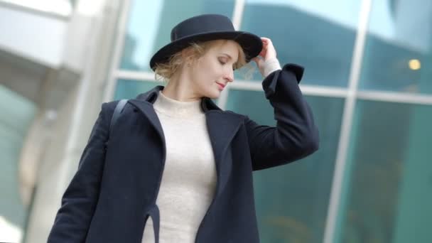 Женщина играет с современной черной шляпой движущейся широкополой часовни в нижней части черного пальто в уличной замедленной съемке — стоковое видео