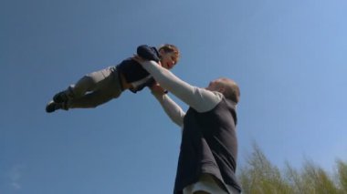 Babam oğlunu yukarı yaslar, çocuk yaz güneşli bir gün. Yavaş Çekim. baba ve oğlu açık havada eğlenmek