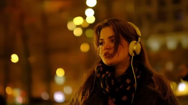 Adolescente avec de longs cheveux marchant le long de la rue, écoutant la musique portant des écouteurs la nuit sous les lumières rouges. Mouvement lent . — Video