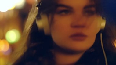 Uzun saçlı sokak boyunca yürüyüş, kırmızı ışıklar altında geceleri kulaklık giyen müzik dinleme ile closeup genç kız. Yavaş hareket.
